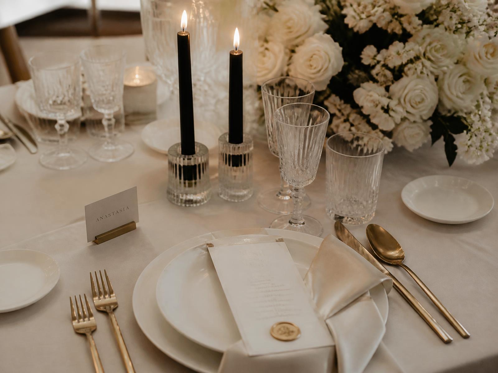 Mesa de casamento posta com louça off-white, talheres dourados e flores brancas